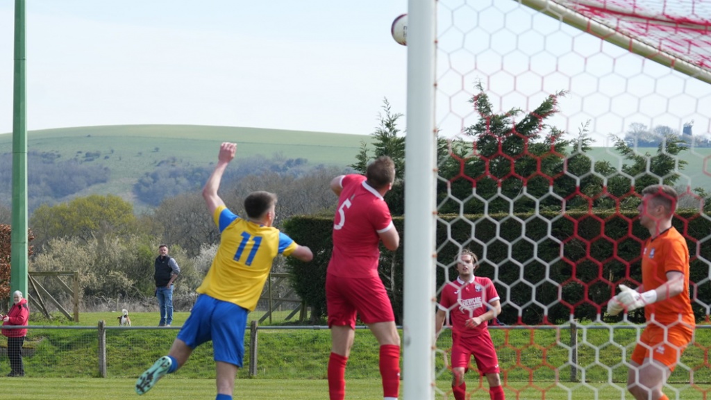 Sam Smith of Hassocks headers away a Eastbourne Town cross into the box