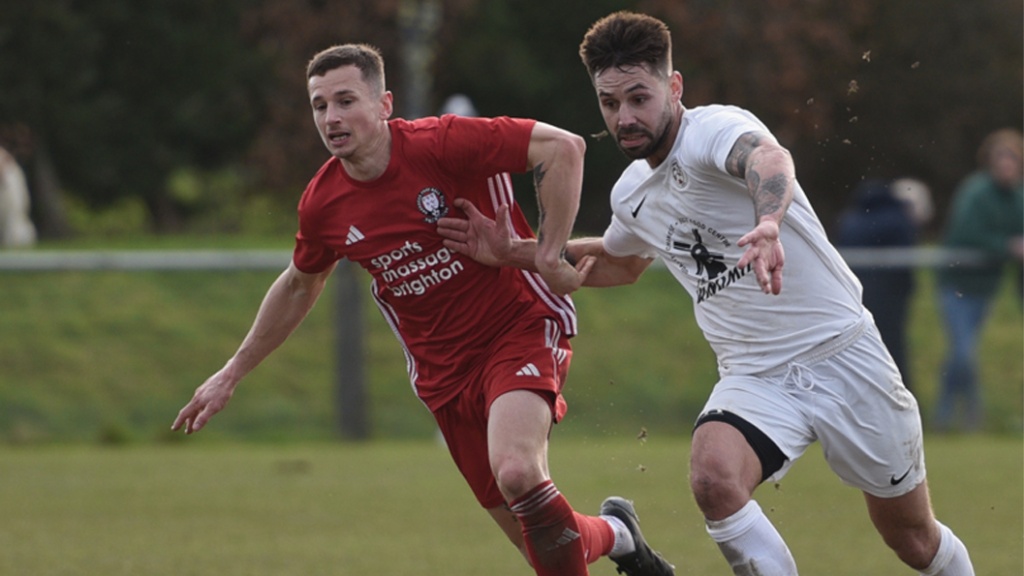 Mike Williamson of Hassocks challenges an Eastbourne United midfielder for possession